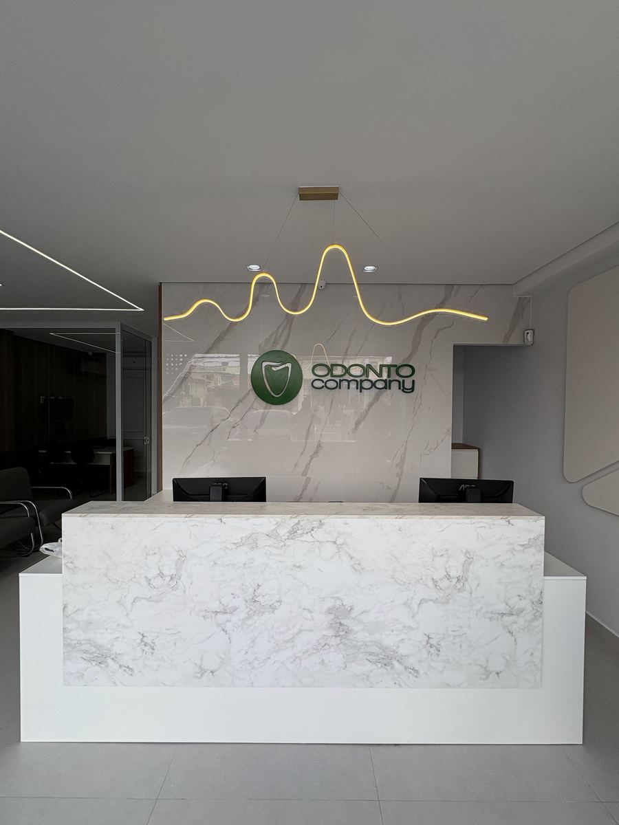 Recepção da OdontoCompany Rio Pequeno, com balcão de mármore e o logo na parede